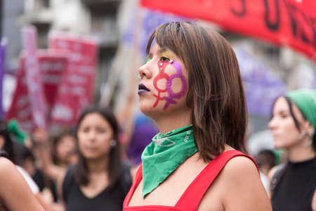 CABA, Buenos Aires / Argentina; March 9, 2020: international women's day. Serious expression young woman, wearing makeup and a green handkerchief, on the march, national women's strikeのeditorial素材