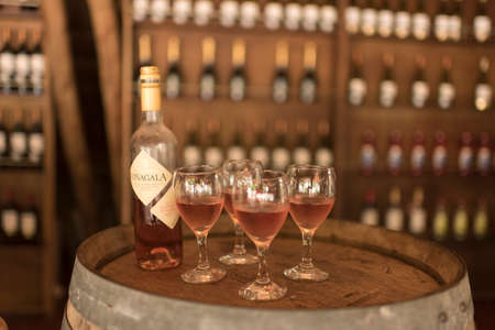 Carmelo, Colonia / Uruguay; Dec 27, 2018: a bottle and four glasses of rose wine, on a barrel,...
