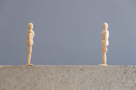 Conceptual image about social distancing, mandatory due to the coronavirus outbreak, covid-19. Pair of wooden human figures standing looking at each other from a safe distance.の写真素材