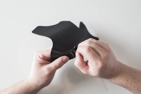 Hands sewing pieces of synthetic leather, making a homemade protective face mask, to prevent the...