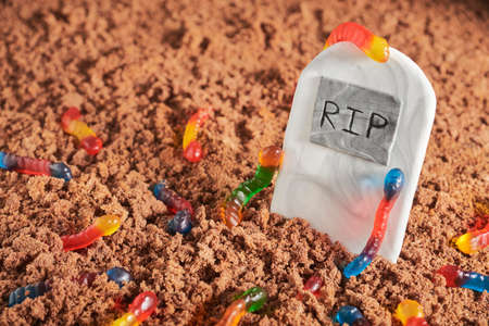 Colorful and bright assorted gummy worms in chocolate cake ground around a sugar gravestone, halloween party fun foodの写真素材