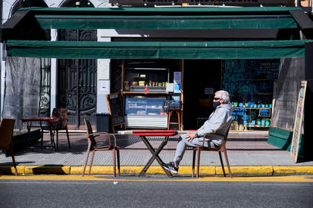 CABA, Buenos Aires / Argentina; Sept 19, 2020: senior man sitting in the sun at a table on the street, wearing a mask, during the coronavirus pandemic, covid-19 outbreakのeditorial素材