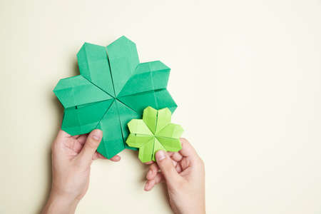 Pair of origami four-leaf clovers, made of green paper, held by two hands of young woman on a light background. Concepts of luck and St. Patrick's Day. Image with copy space.の写真素材
