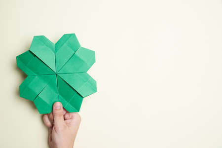 Four-leaf shamrock made of paper, origami, held by a hand of a young woman on a light background. Concepts of luck and St. Patrick's Day. Image with copy space.の写真素材