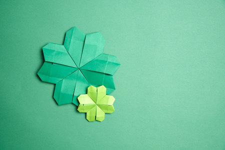 Pair of origami four-leaf clovers, made of green paper, on green background. Concepts of luck and St. Patrick's Day. Image with copy space.の写真素材