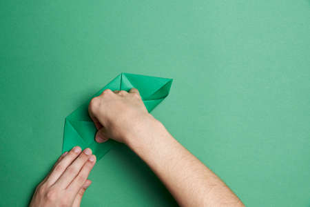 Creation process of an origami clover: young hands folding a green piece of paper, on a green...