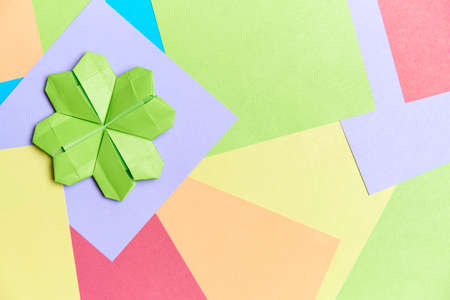 Origami four-leaf clover, light green in color, on a background of square papers of different...