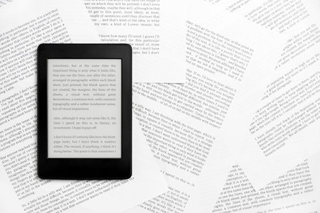 Electronic reader with the screen on and a text on it, on sheets of paper with text printed on them....