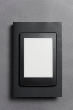 Electronic reader with blank screen over a closed black traditional book, on a gray background. Concepts of technology, modernity and reading. Flat lay image with copy space.の写真素材