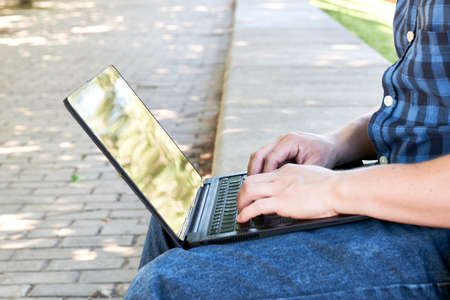 Unrecognizable young man typing on a laptop outdoors. Concept of digital nomad, working or studying...