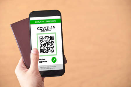 Hand holding a passport and a smartphone with a Covid19 immunity certificate on the screen. Concept...