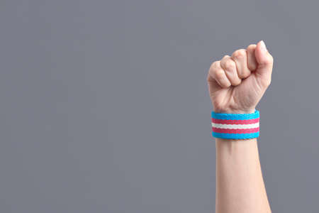 Raised fist of a young person wearing a transgender flag bracelet. Concepts of pride, identity and...