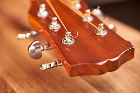 Guitar headstock on a wooden surface. Close-up horizontal image with selective focus.