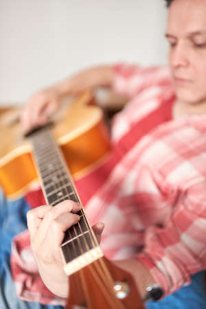 Young hispanic man playing guitar at home. Concepts of music, hobbies and tranquility. Selective...