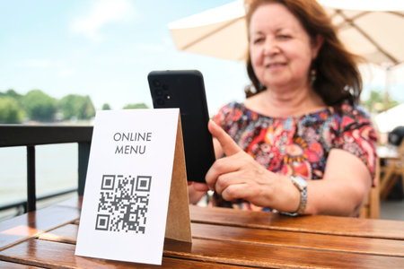 Mature latin woman scanning a QR code to access a restaurant menu; use of contactless technology in everyday life.の写真素材