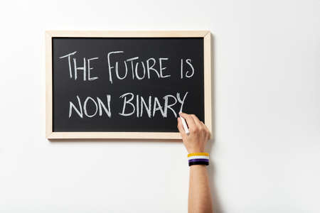 Hand with symbolic bracelet chalking the text The future is non binary on a blackboard. Concept of respect for gender diversity.の写真素材