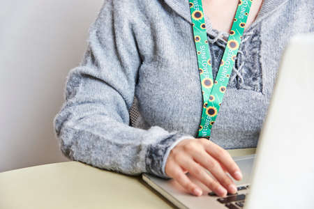 Unrecognizable person studies or works at home with a laptop using a sunflower lanyard, symbol of...