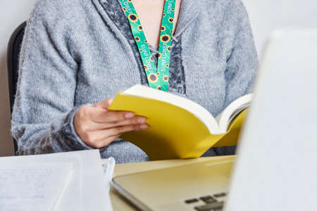 Unrecognizable woman reading a yellow book, studying or working at home, wearing a sunflower...