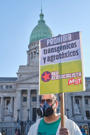 Buenos Aires, Argentina; May 21, 2022: activist wearing biohazard mask and suits holds a sign against the use of GMOs and toxic pesticides in agriculture, in front of the National Congress.のeditorial素材