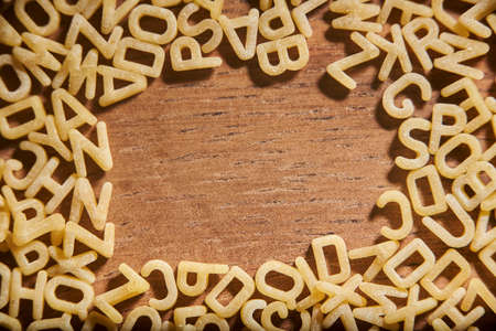 Frame of alphabet soup pasta letters on a wooden background. Concepts: healthy mediterranean food, carbohydrates diet, reading and education.の写真素材