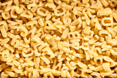 Uncooked alphabet soup pasta letters background. Concepts: healthy mediterranean food, carbohydrates diet, fun education.の写真素材