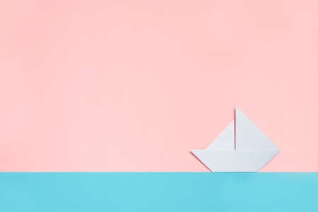Origami boat sailing through a minimalist paper light blue and pink landscape. Minimal summer and travel concept, trendy bright pastel colors, background with copy space.の写真素材