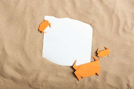 Fun flat lay composition on the concept of summer, beach and vacations, smooth sand background with a family of origami crabs and a blank paper card. Creative layout, minimal design with copy space.の写真素材
