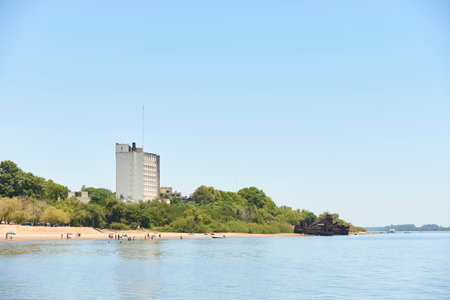 Dec 30, 2021, Colon, Entre Rios, Argentina: beach as seen from a boat on the Uruguay river, people enjoying the shore, Intersur hotel and abandoned rusty ships.のeditorial素材