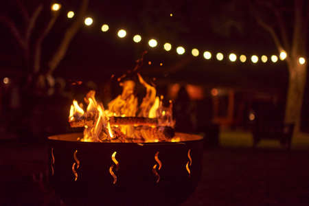 Bonfire burning in a garden on a warm summer night, unrecognizable people in the background. Concepts: coziness, travel, enjoyment of the outdoors.の写真素材