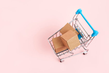 Shopping cart with cardboard boxes on a pastel pink background. Top view composition with copy space. Concepts: market sales, seasonal discounts, logistics, packaging.の写真素材