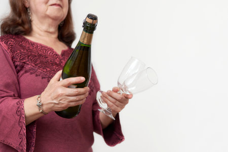 Hispanic mature woman holding a bottle of champagne or cider and a pair of glasses. Concept of celebratory toast. Selective focus composition with copy space.の写真素材