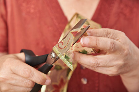 Hands of an unrecognizable mature woman cutting a decorative Christmas ribbon with scissors. Close-up composition.の写真素材