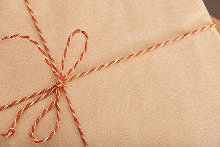 Top view of a Christmas gift wrapped in neutral paper and tied with a red and gold decorative string. Simple close up image with copy space.の写真素材