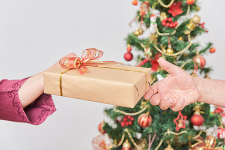Hands of unrecognizable adult couple celebrating the holidays at home, she gives him a Christmas...