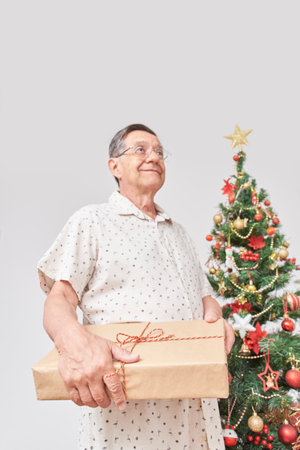 Senior Hispanic man smiling while holding a Christmas present. Concept: the joy of gift giving during the holidays. Vertical composition with selective focus and copy space.の写真素材