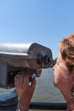 Close up view of a mature latin woman viewing through public binoculars. Concepts of curiosity, observation, exploration, research, travel.の写真素材