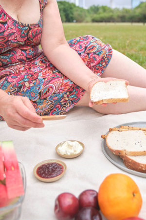 Unrecognizable woman enjoying a healthy breakfast picnic with whole grain bread and assorted fruits.の写真素材