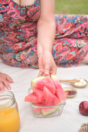 Unrecognizable woman grabbing a slice of watermelon during a picnic breakfast. Concepts: healthy lifestyle, enjoying the outdoors in summer.の写真素材