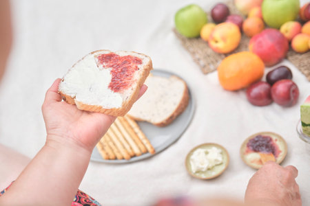 Unrecognizable woman enjoying a healthy breakfast picnic with whole grain bread and assorted fruits.
