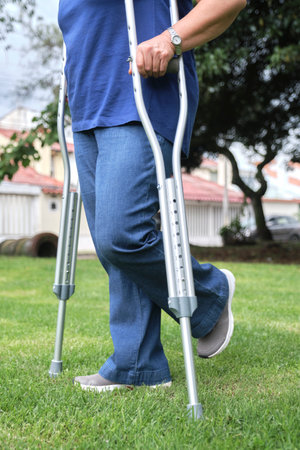 Unrecognizable woman walking with the help of crutches in an urban park. Side view with copy space.の写真素材