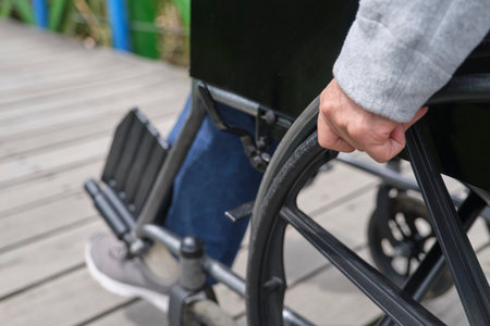 Unrecognizable woman strolling in a wheelchair, outdoors. Close up of a female hand moving the wheelchair forward.の写真素材