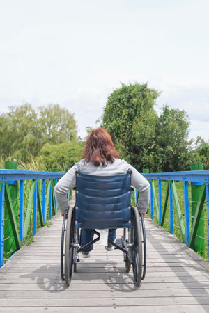 Back view of an unrecognizable woman strolling in a wheelchair, outdoors. Vertical image with copy space.の写真素材
