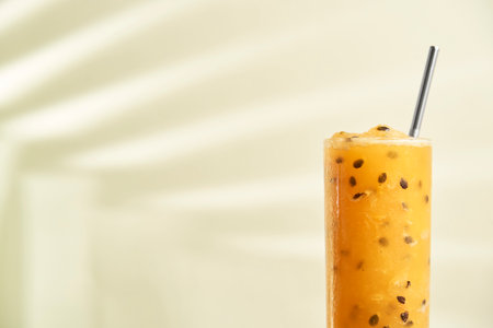 Glass of a yellow refreshing passion fruit drink, juice or cocktail, with a reusable ecological straw. The shadow of a tropical leaf is projected on the back wall.の写真素材