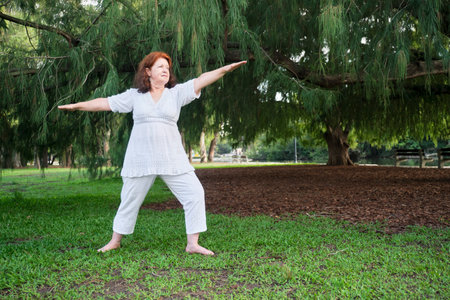 Portrait of a mature Hispanic woman in white clothes practicing yoga outdoors in a park. Concepts: wellness, vitality, active and healthy lifestyle.の写真素材