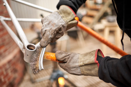 Unrecognizable worker with workwear including protective gloves using a wire brush over a bicycle...