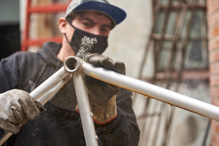 Hispanic worker removing the paint from a bicycle frame as part of the process of a bike renovation work made at his workshop. Selective focus composition with copy space.の写真素材