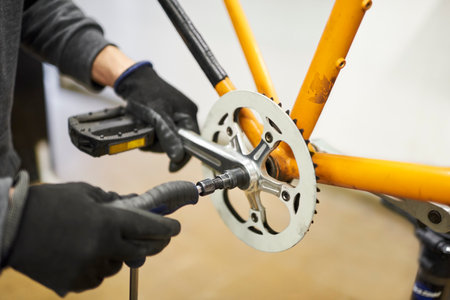 Maintenance of a bicycle: hands of an unrecognizable person wearing gloves disassembling the pedals of an orange bike at his repair shop.の写真素材