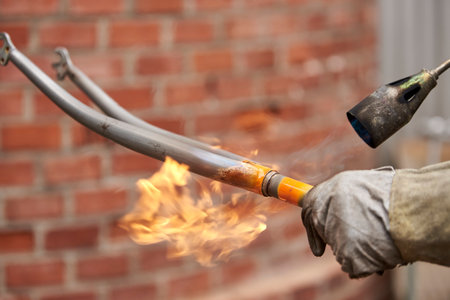 Worker hand with protective glove. Use of a blowtorch to remove the paint from an orange fork from a bicycle that is being renovated in a bike workshop.の写真素材