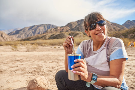 Happy latin woman having a hot drink for breakfast at mountain camp, a sunny morning. Composition with copyspace.の写真素材