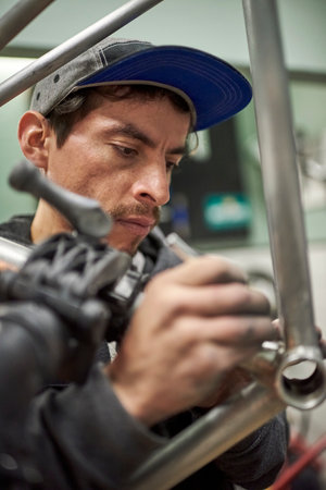 Hispanic man removing paint residue from a bicycle frame as part of the process of a bike renovation...